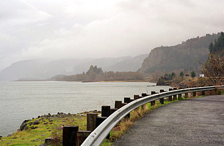 [The guard rail separating the parking area from the slight drop into the river is on the right of the image. Several hillsides, each more shrouded in mist the further in the distance they are, are also along the right although the furthest one crosses the entire image due to the river's curve.]